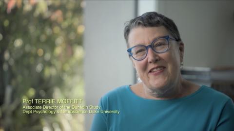 Moffitt sits for an interview facing slightly off camera in a blue-green top. Background is fuzzy and features a room with a large window and plenty of natural light.